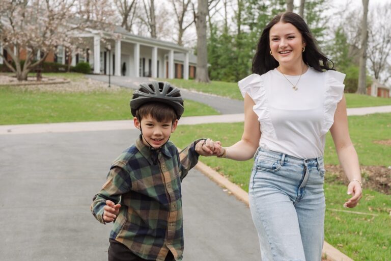 Sitter holding hands with a boy learning to rollerblade